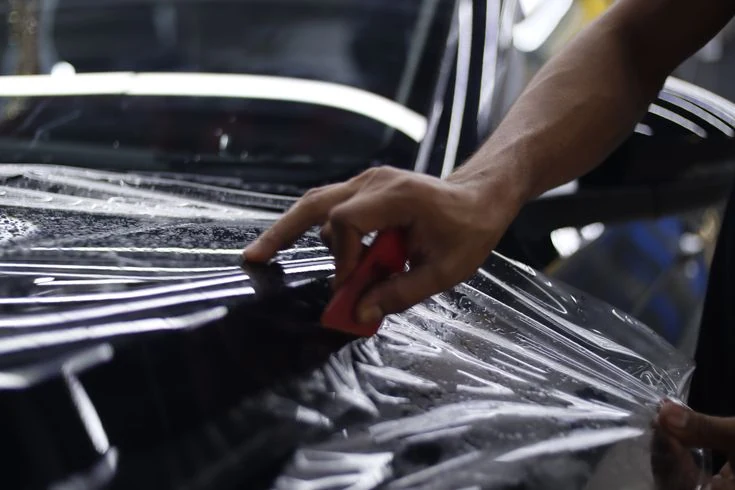 Technician installing Paint Protection Film clear bra on sports car front end